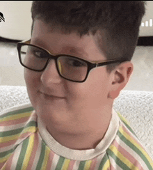 a young boy wearing glasses and a striped shirt is smiling while sitting on a couch .
