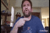a man with a beard wearing a blue shirt is pointing at something .