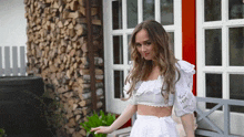 a woman in a white crop top and skirt is standing in front of a pile of logs