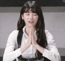a woman in a white shirt and black vest is praying with her hands folded .