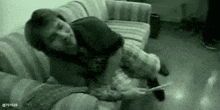 a black and white photo of a man laying on a couch holding a piece of paper .