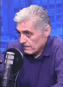a man in a purple shirt is sitting in front of a microphone that says me