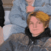 a young man with blonde hair is wearing a denim jacket and a black hoodie