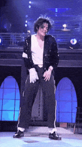 a man in a black jacket and white shirt is dancing on stage