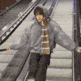 a person wearing a hoodie and a scarf is walking down an escalator .