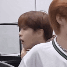 a man with red hair is sitting next to another man in a white shirt and talking on a cell phone .