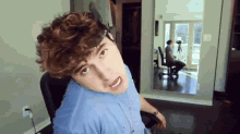 a man with curly hair is sitting in a chair and making a funny face