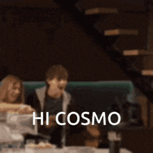 a blurred image of people sitting at a table with the words hi cosmo on the bottom right