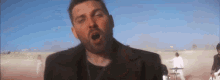 a man with a beard is singing in front of a group of people in a desert .