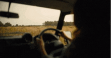 a person is driving a car on a dirt road with a field in the background .