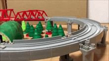 a toy train track with trees and a bridge in the background