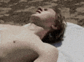 a shirtless young man is laying on a white towel on the beach .