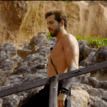 a shirtless man with a tattoo on his arm is standing on a rocky beach