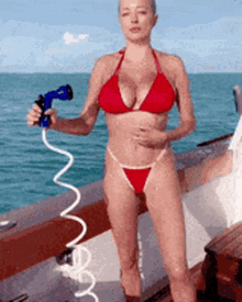 a woman in a red bikini is holding a hose in front of the ocean