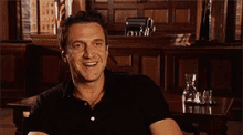 a man in a black shirt is smiling while sitting at a table
