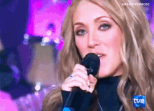 a close up of a woman singing into a microphone with a tvb logo in the background