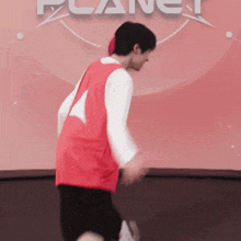 a man in a red shirt and black shorts is playing tennis in front of a sign that says planet