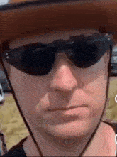a man wearing a cowboy hat and sunglasses is looking at the camera .