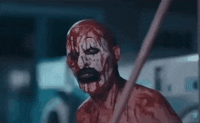 a bloody clown with blood on his face is waving his hands in a dark room .