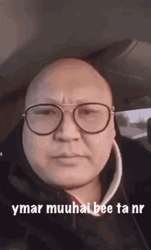 a bald man wearing glasses is sitting in a car