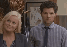 a man and a woman are standing next to each other in an office . the man is wearing a striped shirt and tie .