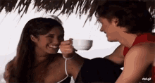 a woman is feeding a cup of coffee to a man .