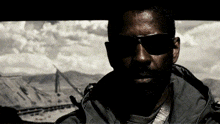 a man wearing sunglasses looks at the camera with a mountain in the background