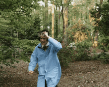 a man in a blue lab coat and goggles is walking through a forest