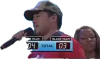 a man singing into a microphone with a scoreboard behind him that says black team 04 total 03