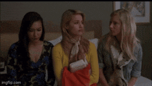 three women are sitting next to each other on a bed in a room .