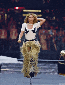 a woman in a white top and gold fringe pants is dancing on a stage