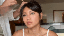 a woman is getting her hair done by a man in a white tank top .