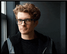 a man wearing glasses and a black hoodie looks at the camera