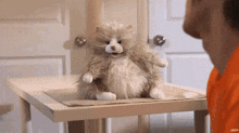 a stuffed animal is sitting on a table next to a man in an orange shirt