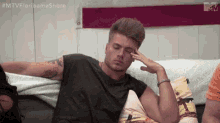 a young man is sitting on a couch with his hand on his forehead .