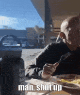 a man sits at a table with a plate of food and a water bottle that says man shut up on it