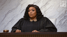 a woman in a judge 's robe sits at a desk in front of a sign that says be on