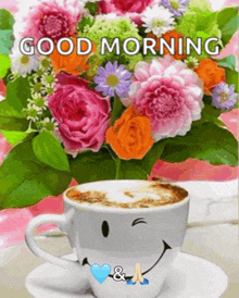 a cup of coffee with a smiley face on it is next to a bouquet of flowers and says good morning
