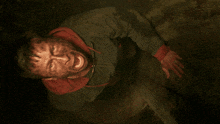 a man in a green jacket with a red hood is screaming in a dark room