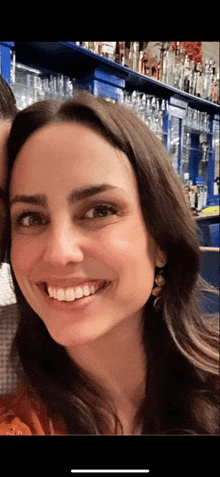 a woman is smiling in front of a bar full of alcohol
