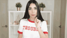 a woman wearing a white shirt that says trouble