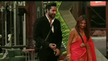 a man and a woman are standing next to each other in a room . the woman is wearing a red saree .