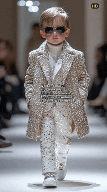 a young boy wearing sunglasses and a coat walks down a runway