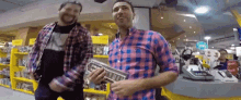 two men in plaid shirts are dancing in a store with a yellow sign that says ' electronics ' on it