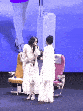 a woman in a white dress stands next to another woman in a white dress in front of an airplane seat that says vat