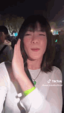 a woman in a white shirt and green wristband is standing in front of a crowd .