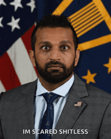 a man in a suit and tie stands in front of an american flag with the words im scared shitless above him