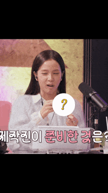 a woman is sitting in front of a microphone with a question mark on it