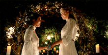 two women are holding hands during a wedding ceremony under a floral arch .