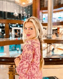 a woman in a pink dress is standing in a mall looking at the camera .